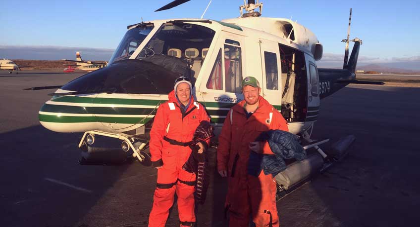 Two people in orange flight suits stand in front of a helicopter