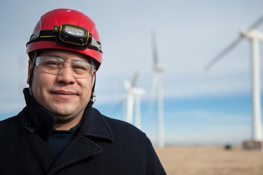 A man in a helmet stands in front of wind turbines.