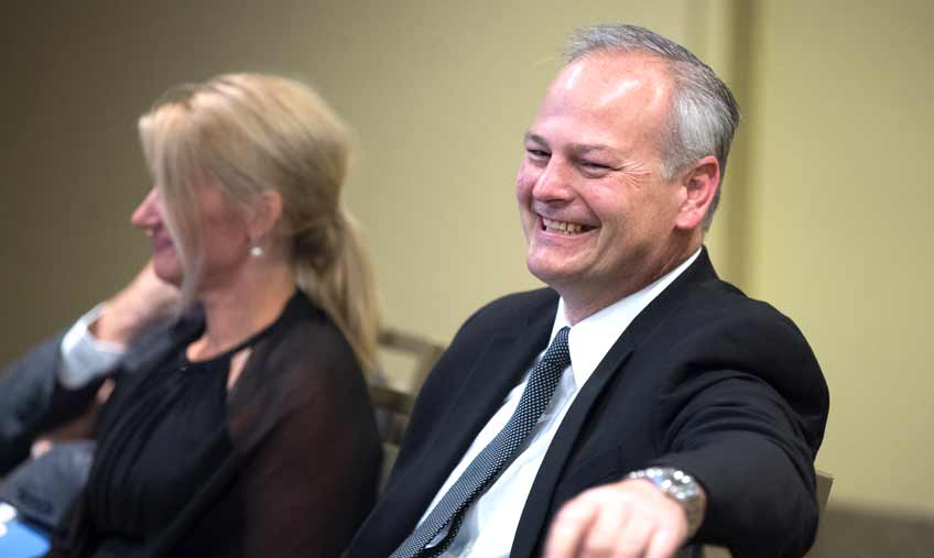 Photo of a man smiling while seated at a table next to a woman.