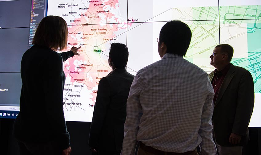 Four researchers view a city map displayed on a large computer screen.