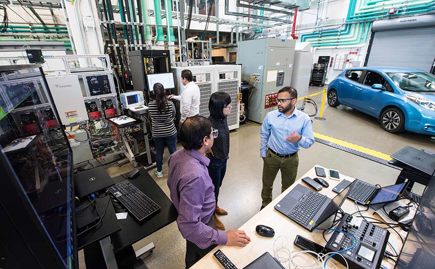 Researchers in a lab with a car in the background