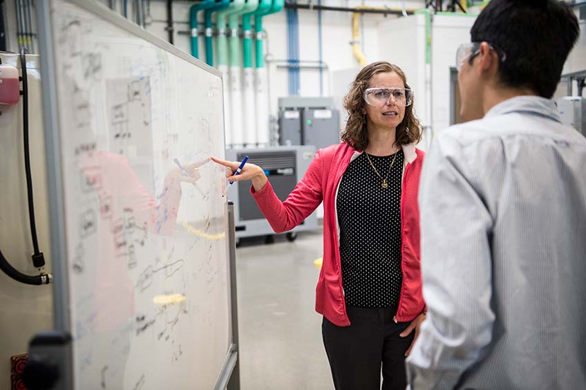 A female researcher explains information written on a white board to a male researcher.