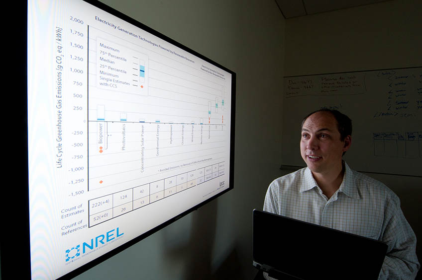 A man holding a laptop views data on a monitor screen.