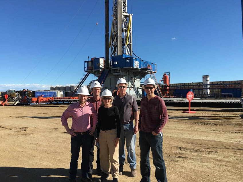 A group of people wearing hardhats stand outside near a natural gas drilling rig.