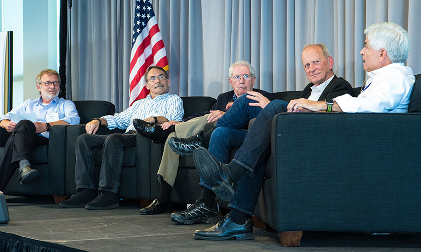 Five men sit on a stage talking