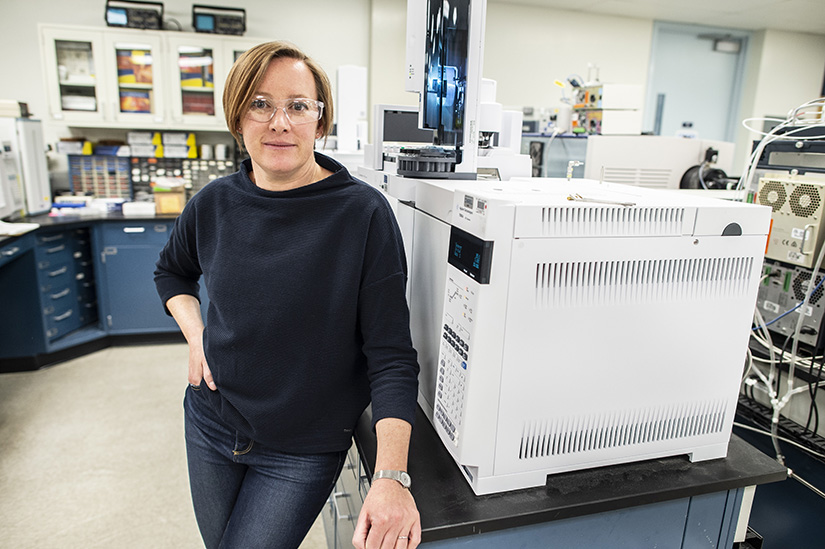 Photo shows a woman standing next to a piece of laboratory equipment.