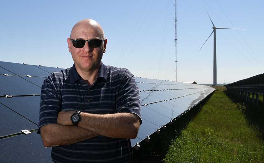 An engineer in front of solar panels and a wind turbine.