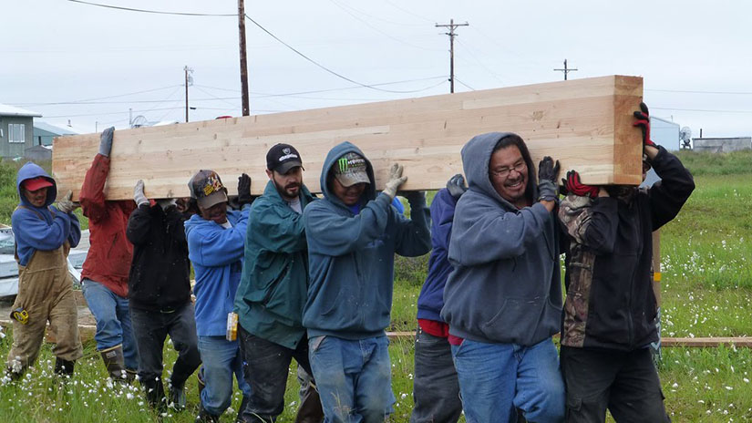 Several men carry a large wooden floor beam outdoors