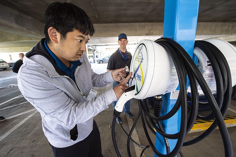 Photo of a man installing electric vehicle charging station equipment in a parking garage.
