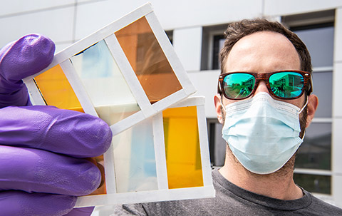 A man holds a prototype of a perovskite window that shows several different colors.