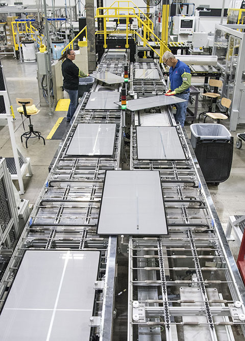 Two workers work on a solar panel production line in a manufacturing plant.