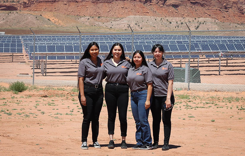 Four women standing in front of a solar array. 