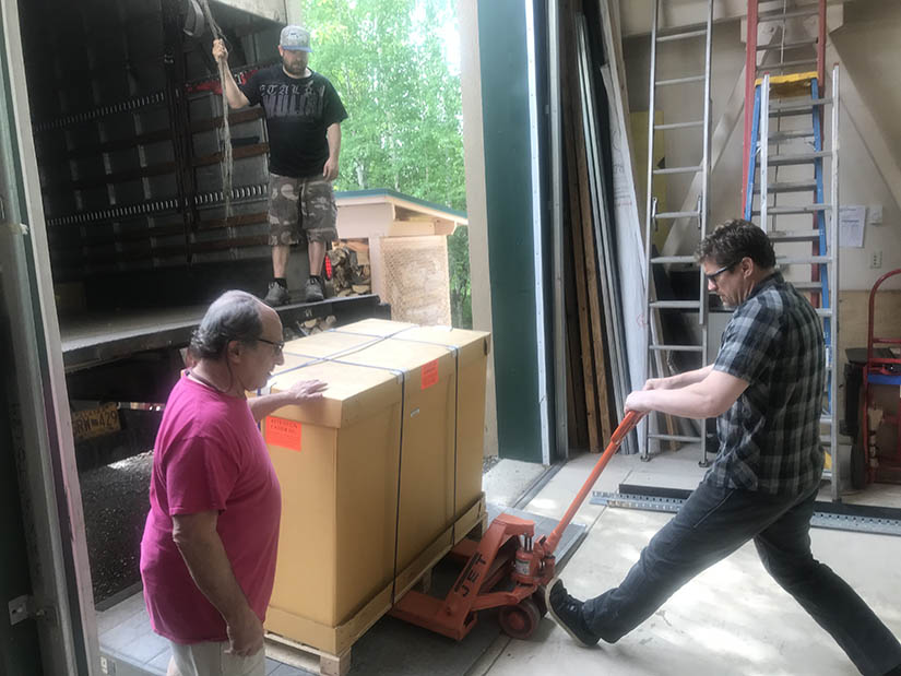 Photo of three people using a dolly to unload a large box from a truck