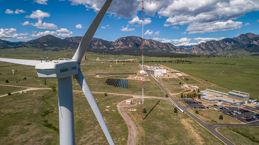 Aerial photo of a renewable energy research campus with wind turbines and solar panels and with mountains and sky in the background