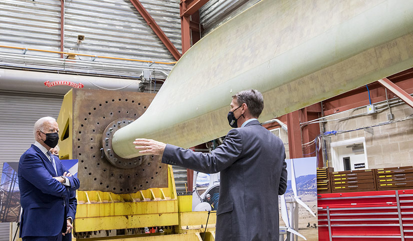 Two people speaking in front of an experimental wind turbine blade in a laboratory facility.