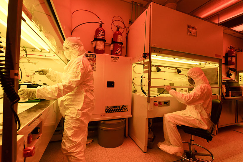 Photo of two researchers wearing clean suits while working in a laboratory lit by orange lights