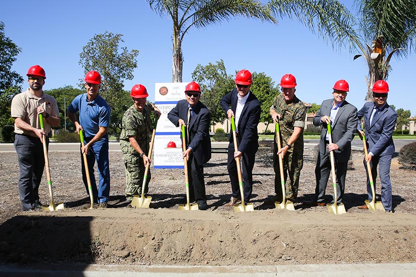Photo of eight people wearing hard hats while breaking ground with shovels.