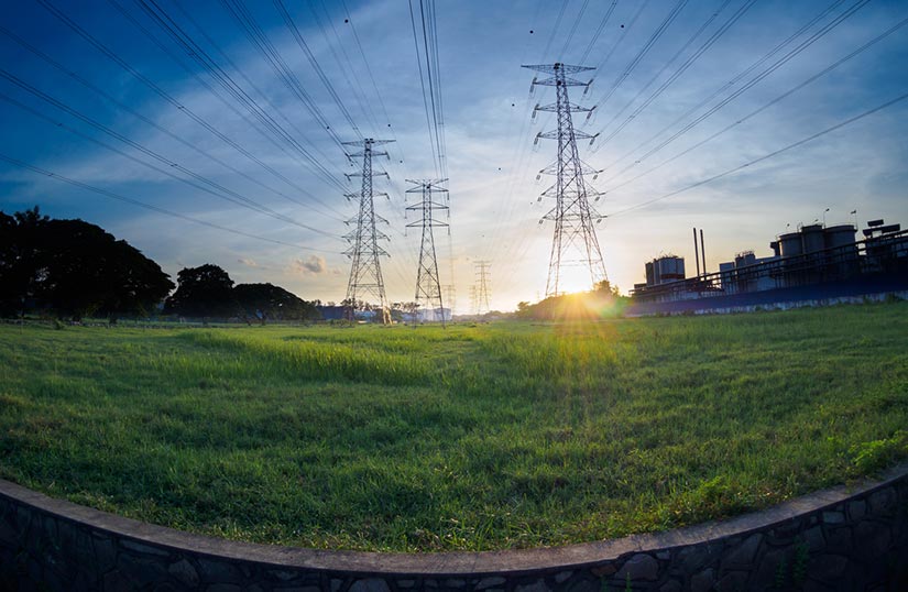 A fisheye image of transmission towers in a grassy field with a blue sky in the backgroun.