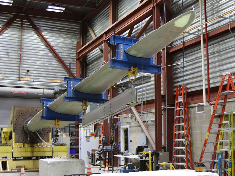Photo of a thermoplastic wind turbine blade in a test device in a warehouse-like building.