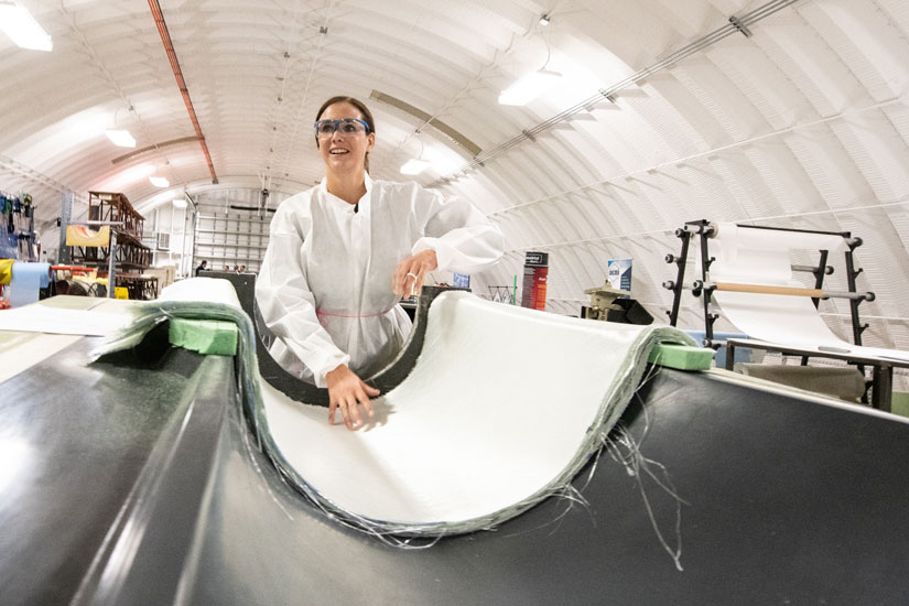 Researcher in a white suit and safety glasses in front of a turbine blade mold.