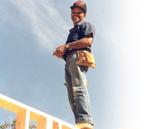 Photo of a man smiling while standing on top of a building frame