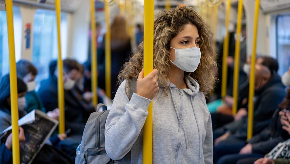 A young woman riding on the metro wearing a facemask