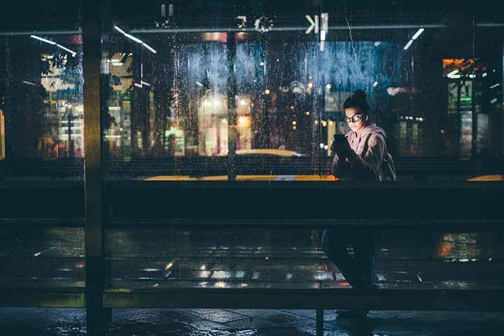 A young woman waiting for public transport inside a modern shelter at night
