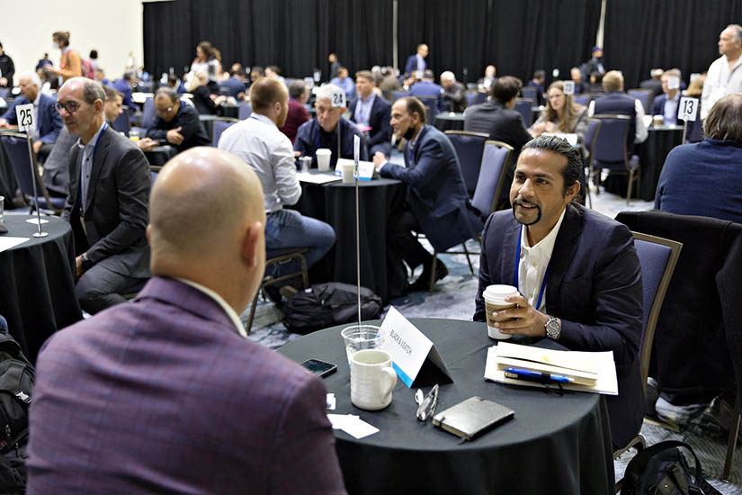 Photo of two people speaking at a table with many other people speaking at separate tables in a large room