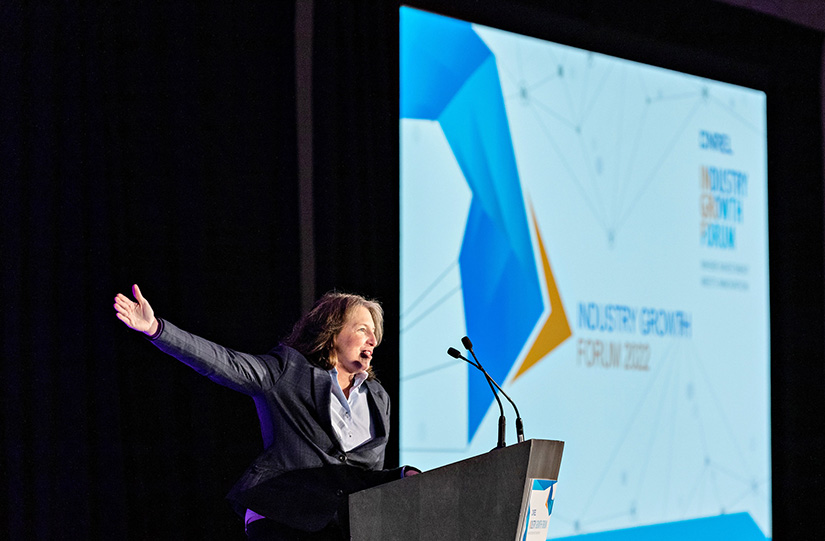 A woman at a podium on an event stage speaks