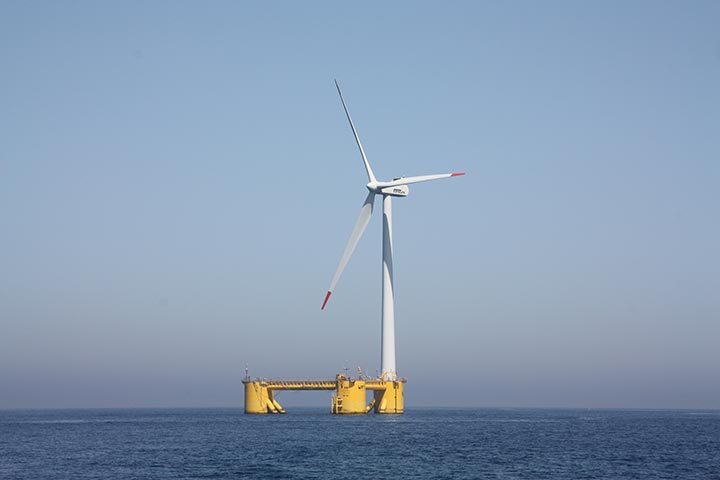 Photo of a wind turbine on a platform atop the ocean.