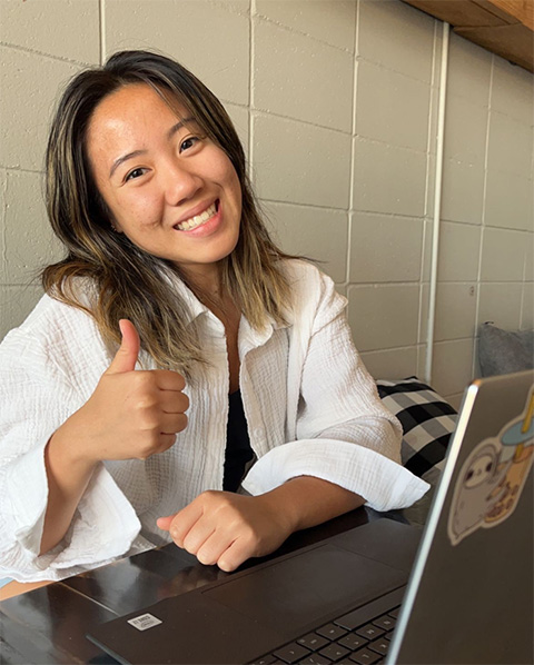 Photo of a woman sitting at a laptop and giving a thumbs-up gesture