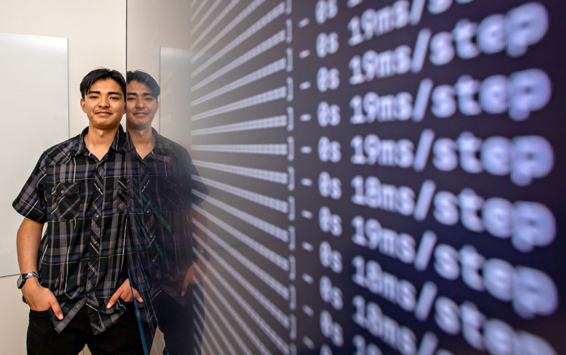 Photo of a man standing next to a computer screen showing lines of code