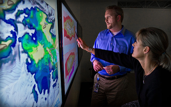 Two researchers point to a screen mapping wind patterns in the U.S. Virgin Islands.