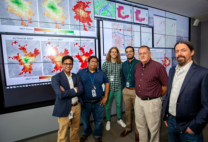 Foto de seis investigadores parados frente a grandes pantallas de visualización de datos.