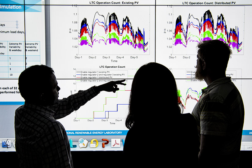 Photo of three people looking at data on a large monitor screen