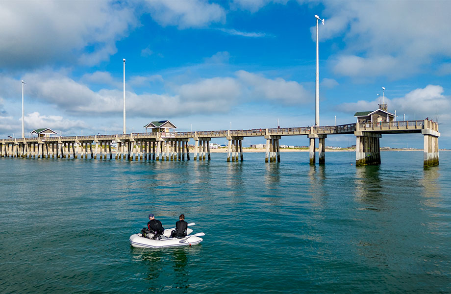 Divers sit in a small boat near a pier.