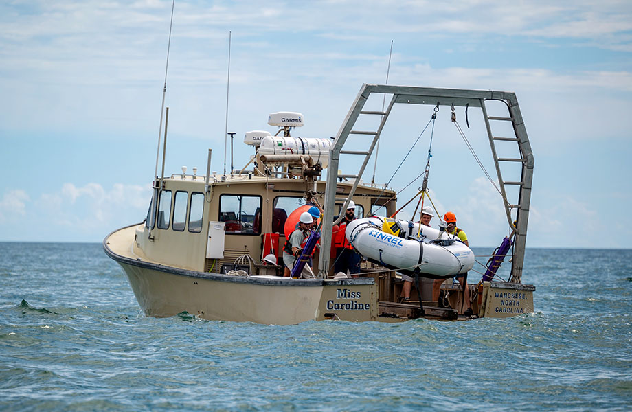 Crew on a boat lower the large WEC device into the sea from the back of the boat (named Miss Caroline).