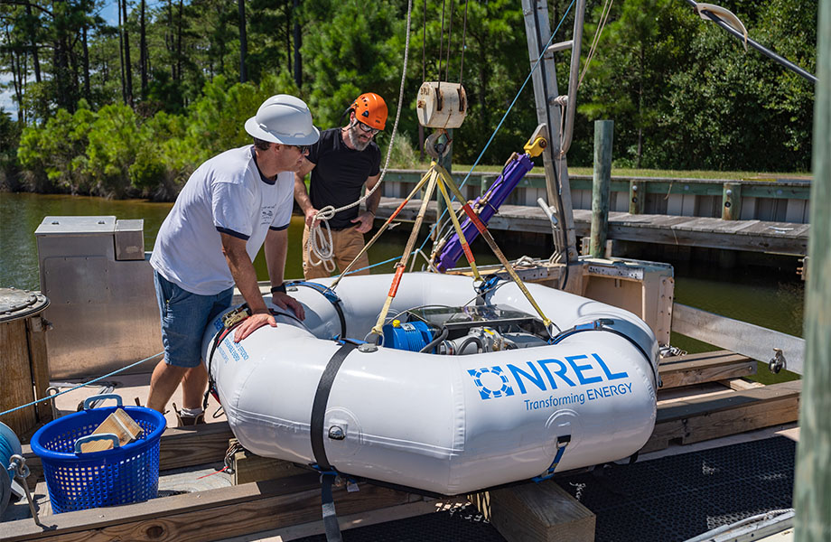 Two men secure the WEC device as it moves from the pier to the boat.