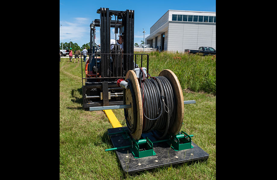A large roll of cable with a forklift behind it.