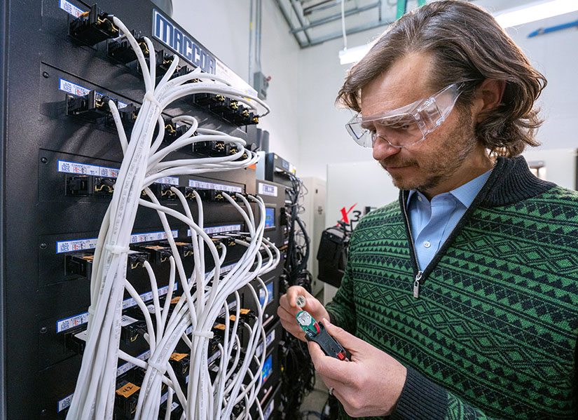 A researcher works with wires and batteries on a laboratory wall.