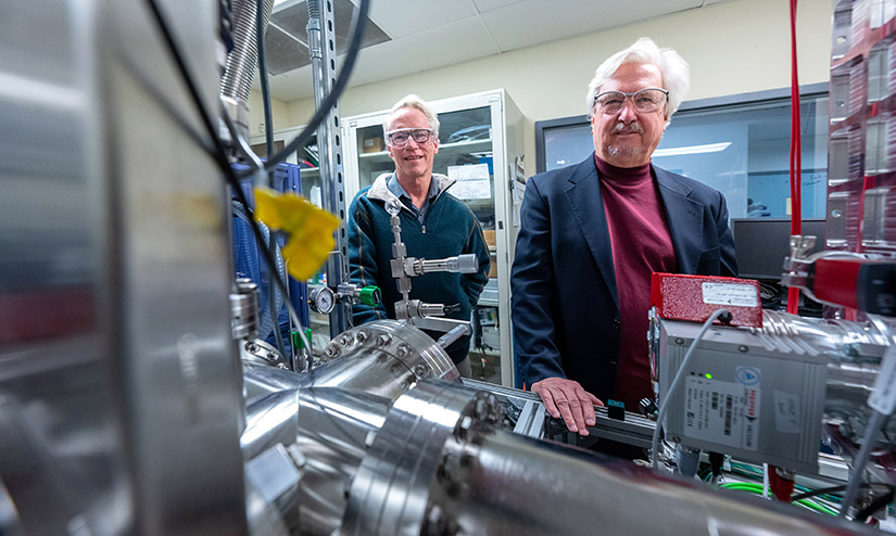 Two men stand amid a cluster of scientific equipment.