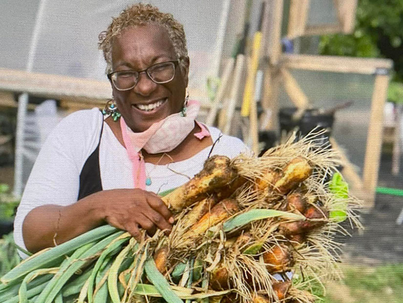 A person smiles and holds crops in their arms.