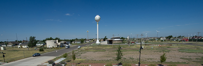 A small town in Kansas, with many empty lots, a water tower in the center, and windmills in the background. 