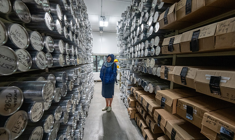 : A woman stands in an aisle surrounded by metal cannisters full of ice core samples. 