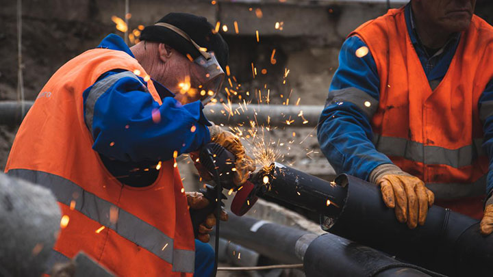 Two men welding a pipe while sparks fly in the air.