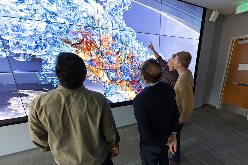 Four people stand in front of a large screen showing a detailed simulation of sustainable aviation fuel as it combusts in a virtual jet engine.
