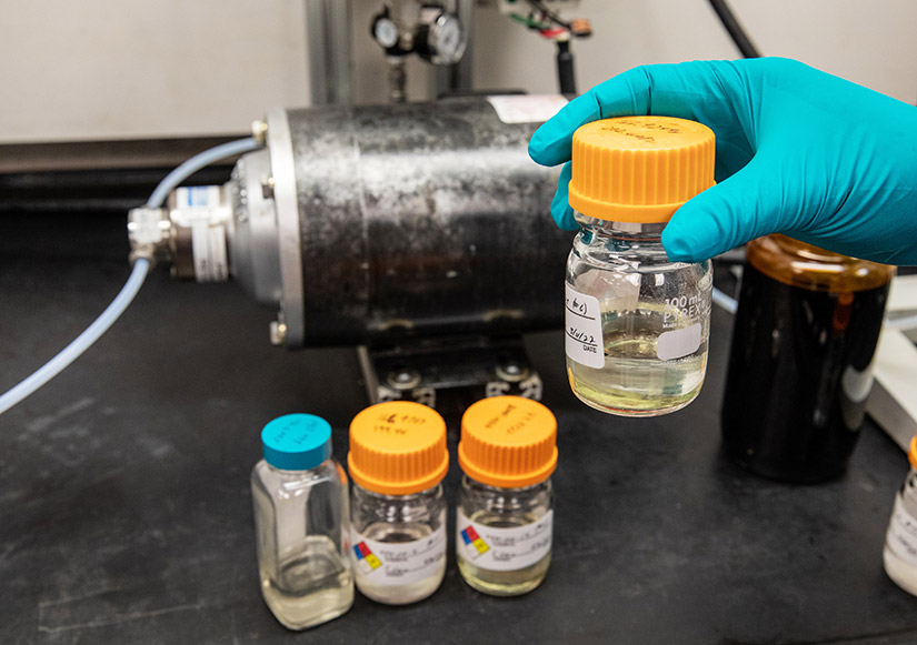 A researcher's hand holds up one of four bottled samples of sustainable aviation fuels.