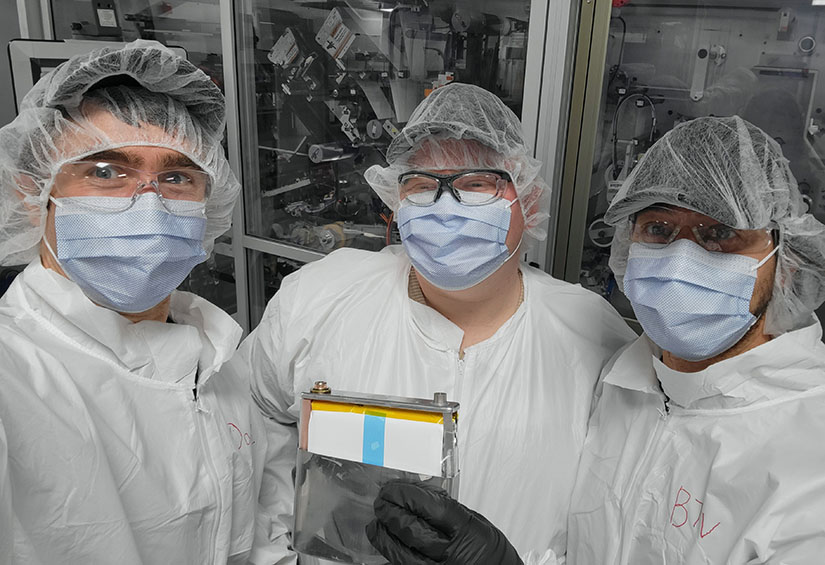 Three researchers wearing PPE hold up a battery.