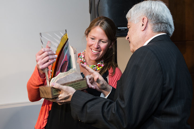 A woman smiles as she is handed a beautiful custom designed glass award.