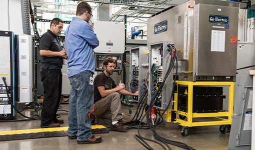 Three engineers work on a Go Electric power inverter in a lab. 